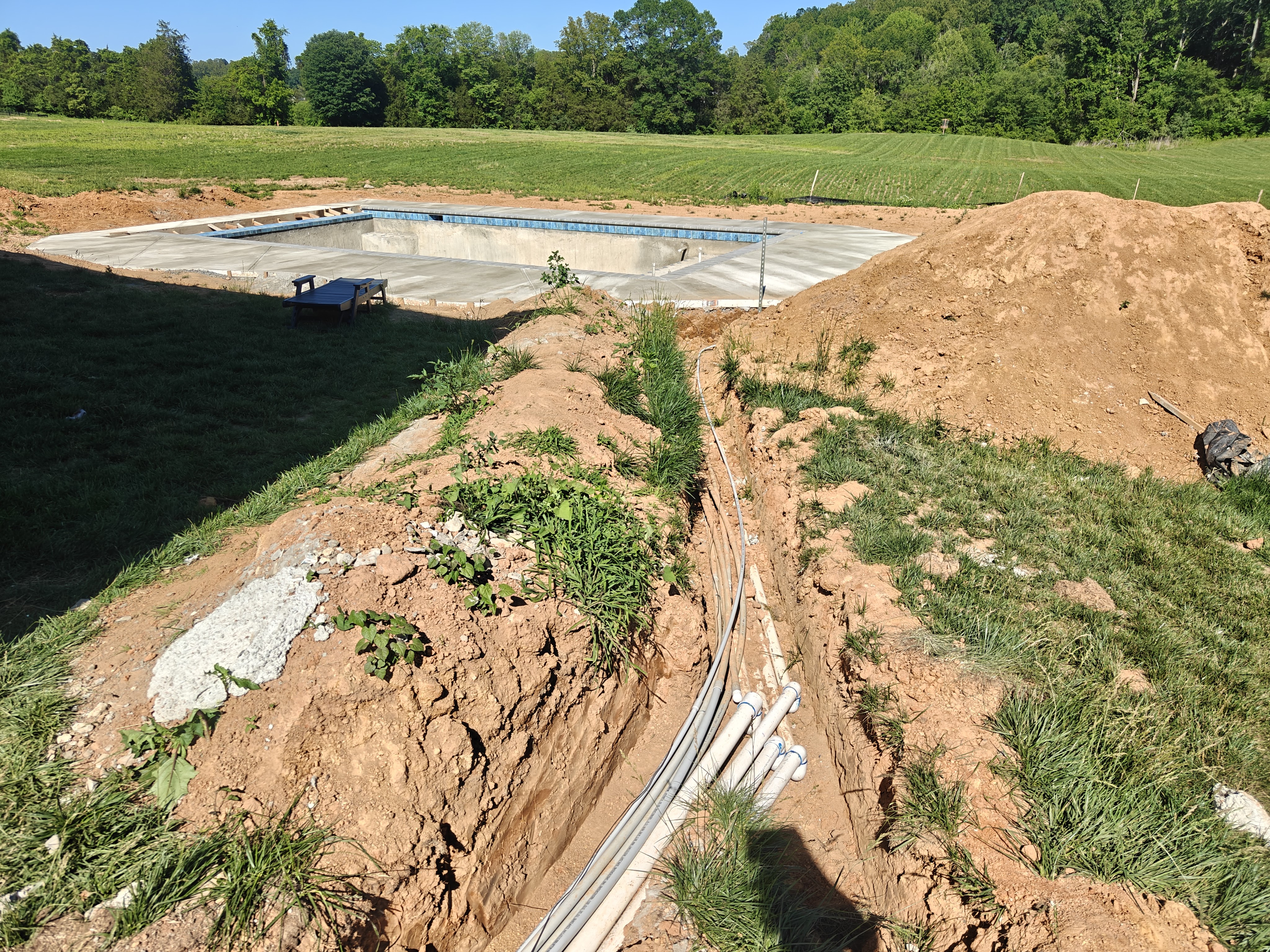 Open trench across a backyard with conduit and an equipotential bonding wire running toward a new gunite pool shell in Stafford, VA