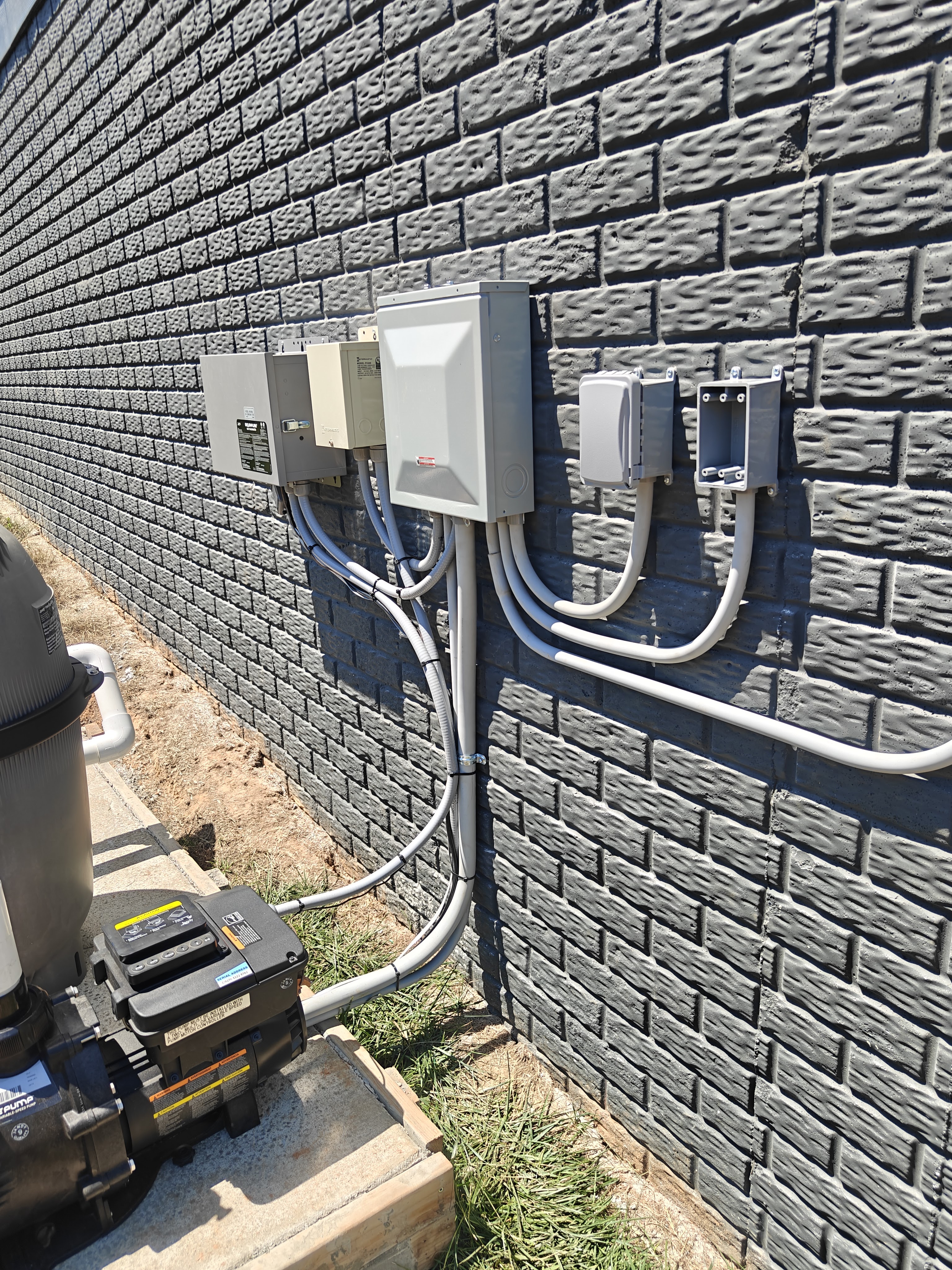 Pool equipment wall in Stafford, VA, with a sub panel, transformer, and junction boxes feeding clean conduit runs down to the pool pump and filter
