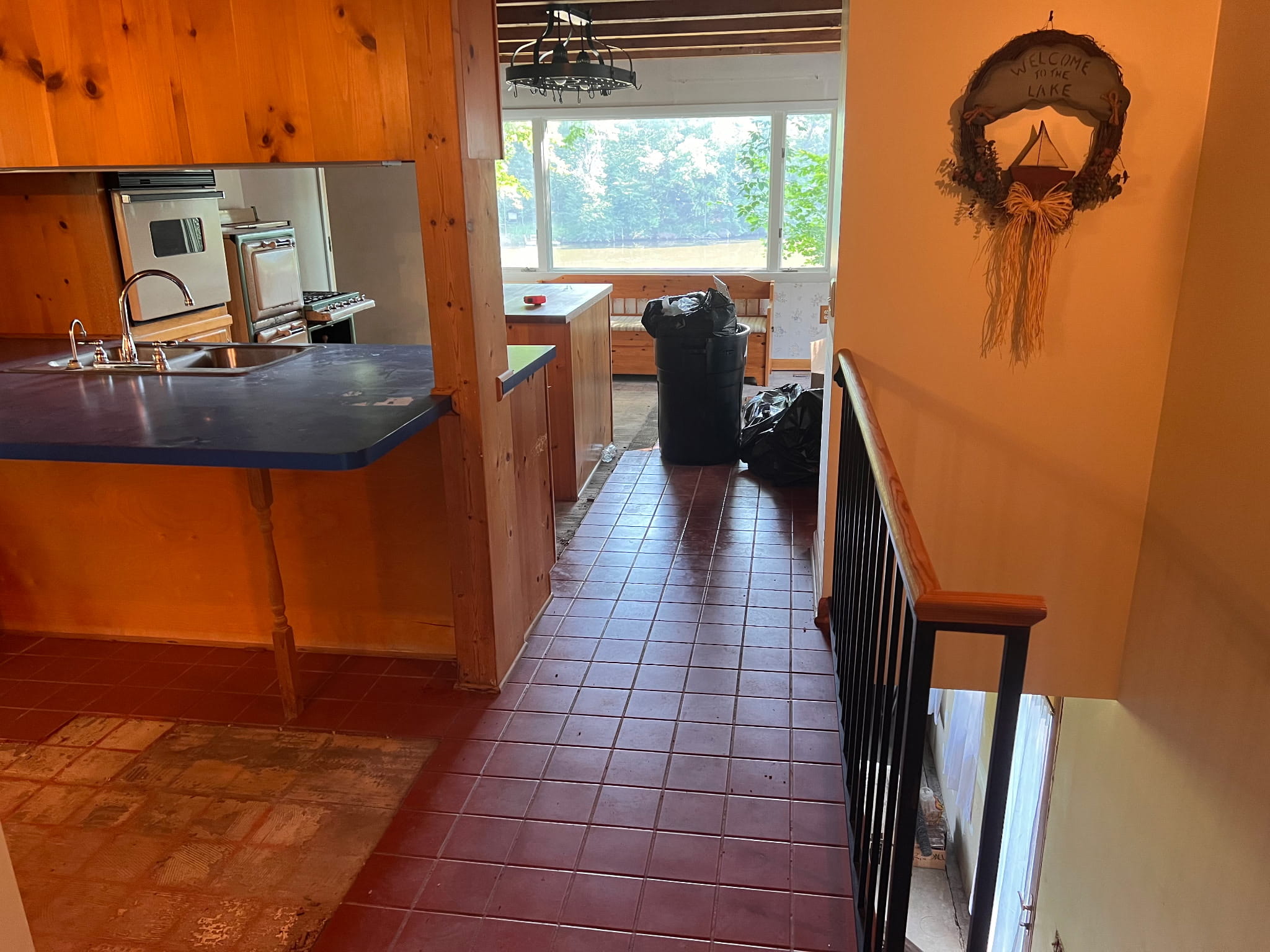 Dated kitchen before remodeling, with knotty-pine paneling and cabinets, a blue laminate peninsula counter, an old wall oven, and red quarry tile flooring