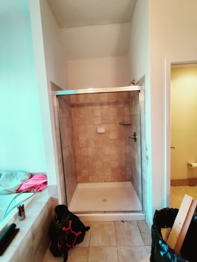 Before: the original cramped shower stall with framed glass, dated square tile, and an acrylic shower pan in a Prince William County master bathroom