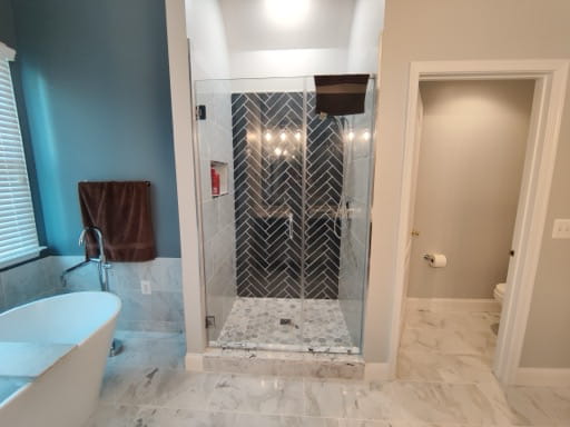 Remodeled master bath with a glass walk-in shower, navy herringbone tile, and freestanding tub