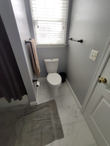 After: the toilet nook with a new toilet, light gray walls, marble-look floor tile, and a matte-black towel bar