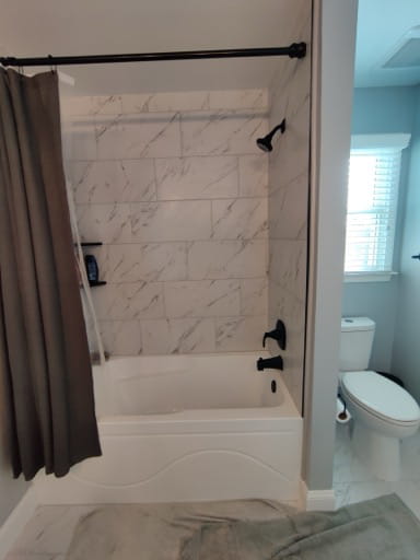 After: a new tub with a marble-look tile surround tiled to the ceiling and matte-black shower fixtures in a Prince William County hall bath