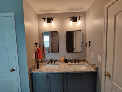 Remodeled hall bathroom with a blue double vanity, granite top, and black fixtures