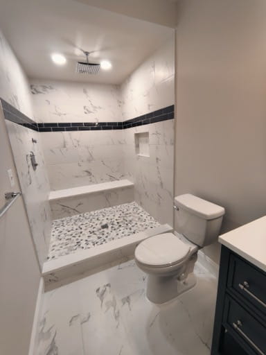 Finished basement walk-in shower with a built-in bench, a recessed niche, a mosaic tile floor, marble-look tile, and a rain shower head