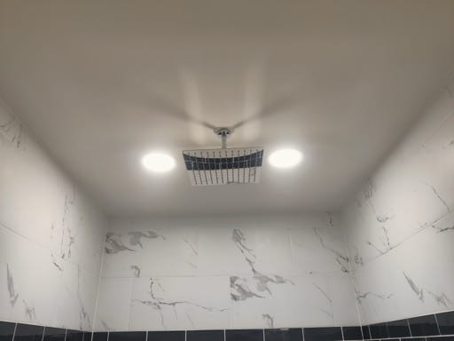 Close-up of the basement shower's ceiling-mounted rain shower head and marble-look large-format tile