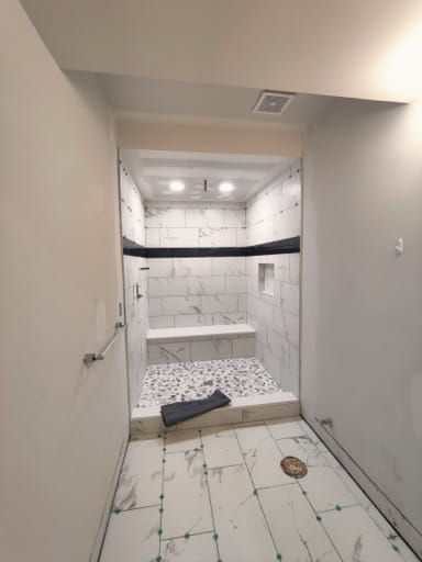 The finished basement bathroom looking toward the curbless tiled walk-in shower with marble-look tile and a dark accent band