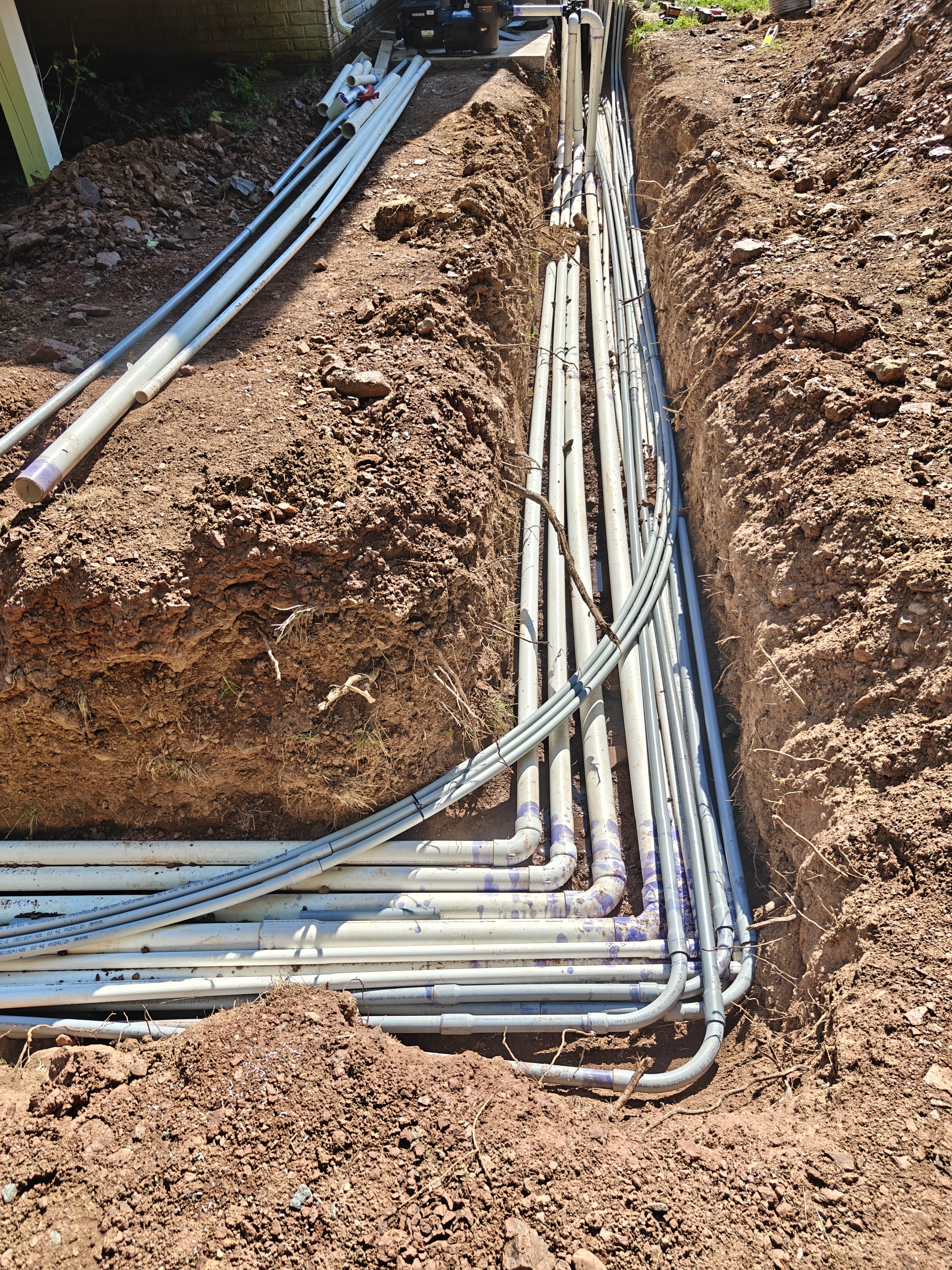 A dense bundle of conduit runs for the pool lights, laminar jets, and equipment sweeping in a neat bend into the trench