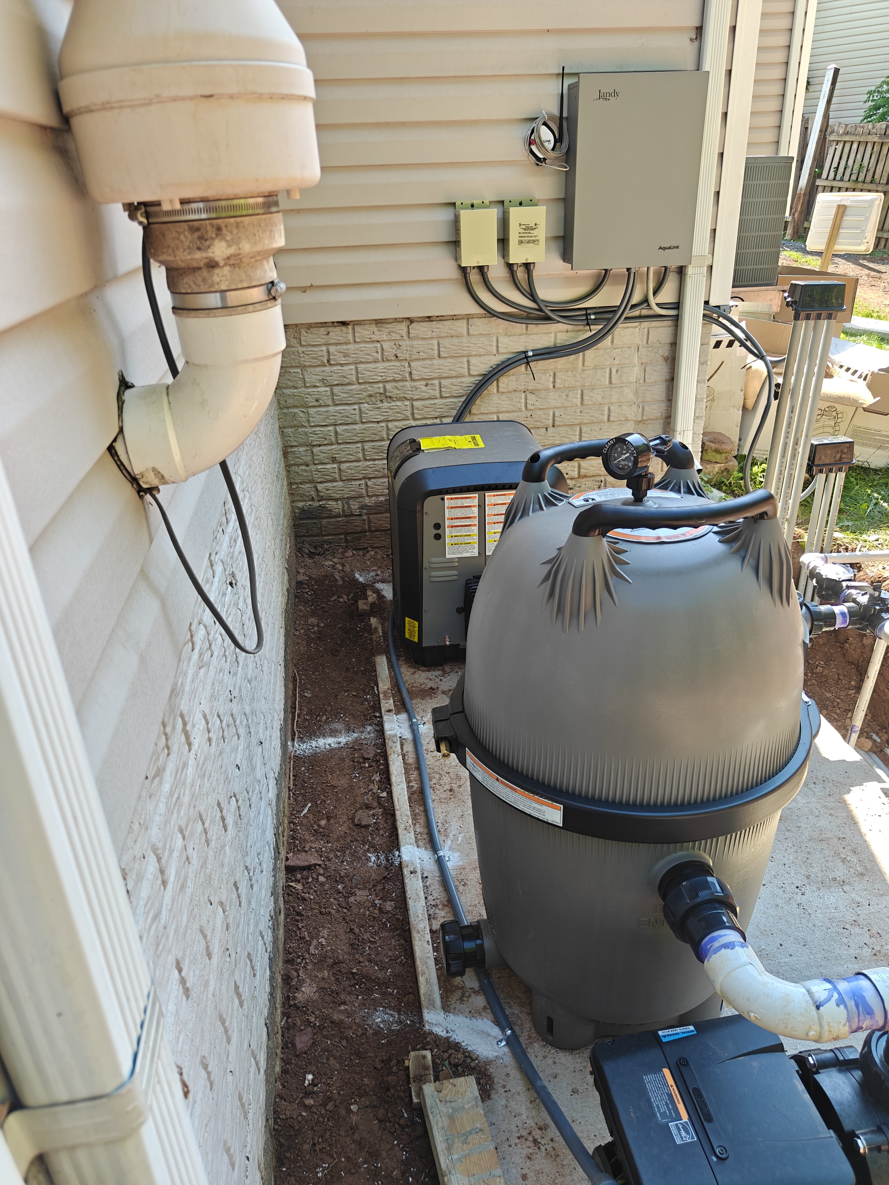 Pool equipment - the Jandy AquaLink panel, two transformers, heater, cartridge filter, and pump - lined up in a narrow side yard along the house in Bristow