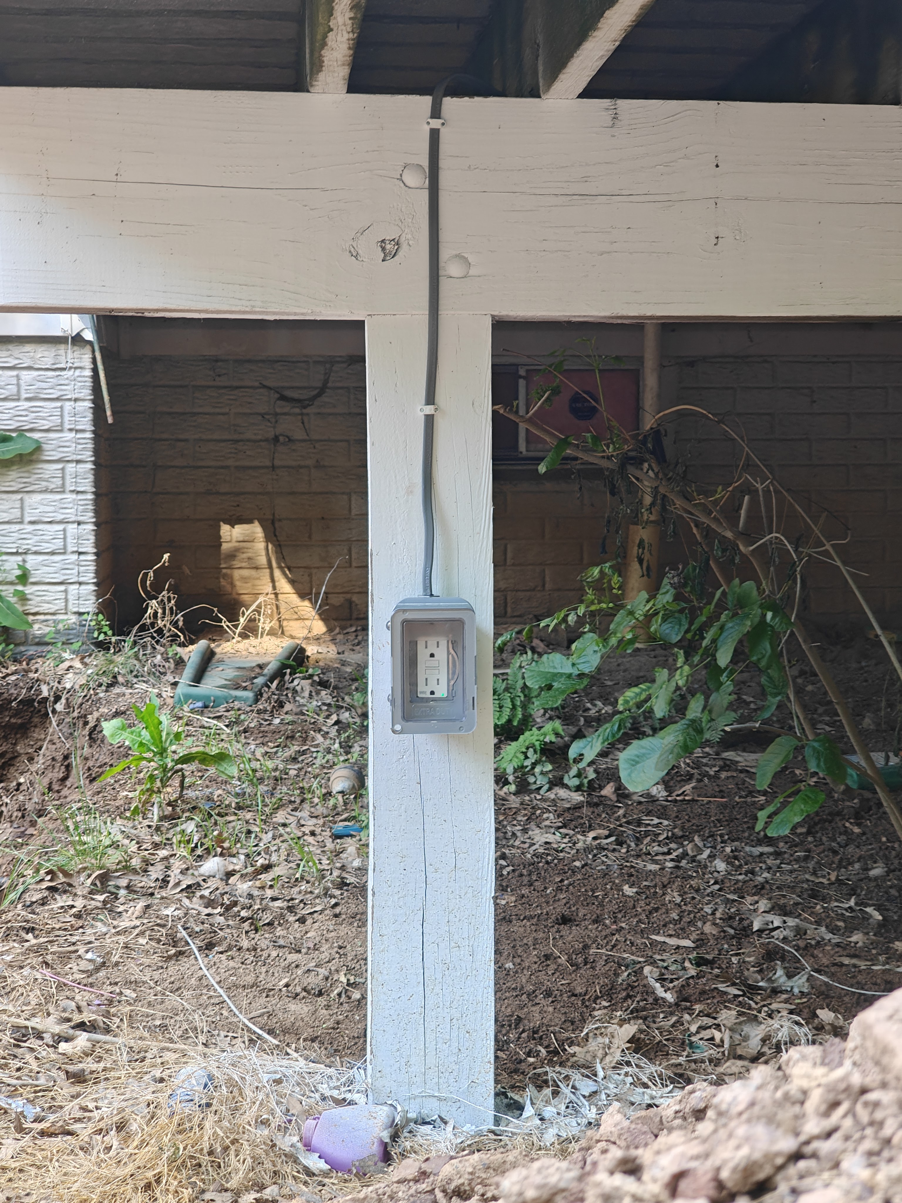 A weatherproof GFCI 6-20 receptacle mounted on a painted deck post, fed by cable run under the deck