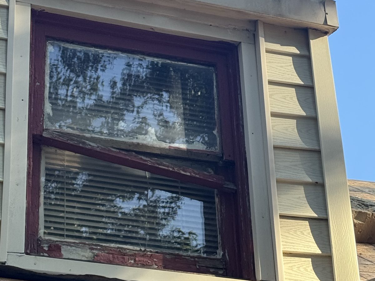 Old wood double-hung window with its meeting rail broken loose and paint worn down to bare wood