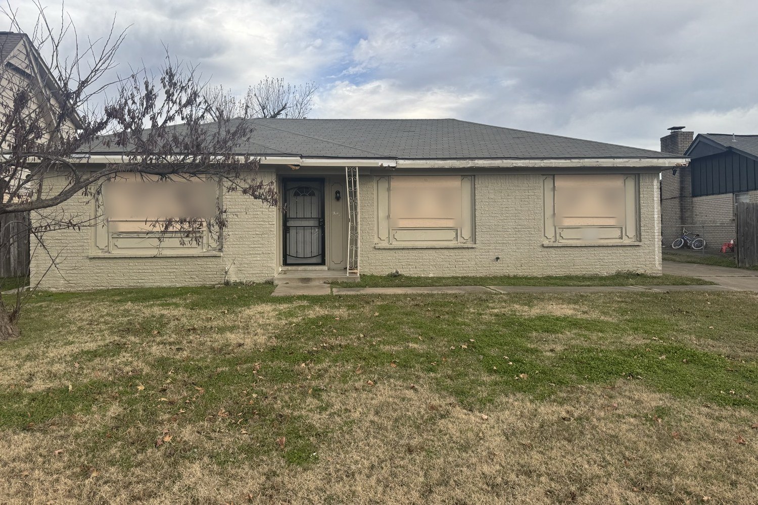Tulsa-area brick ranch house with all three front windows covered by plywood boards, before window replacement