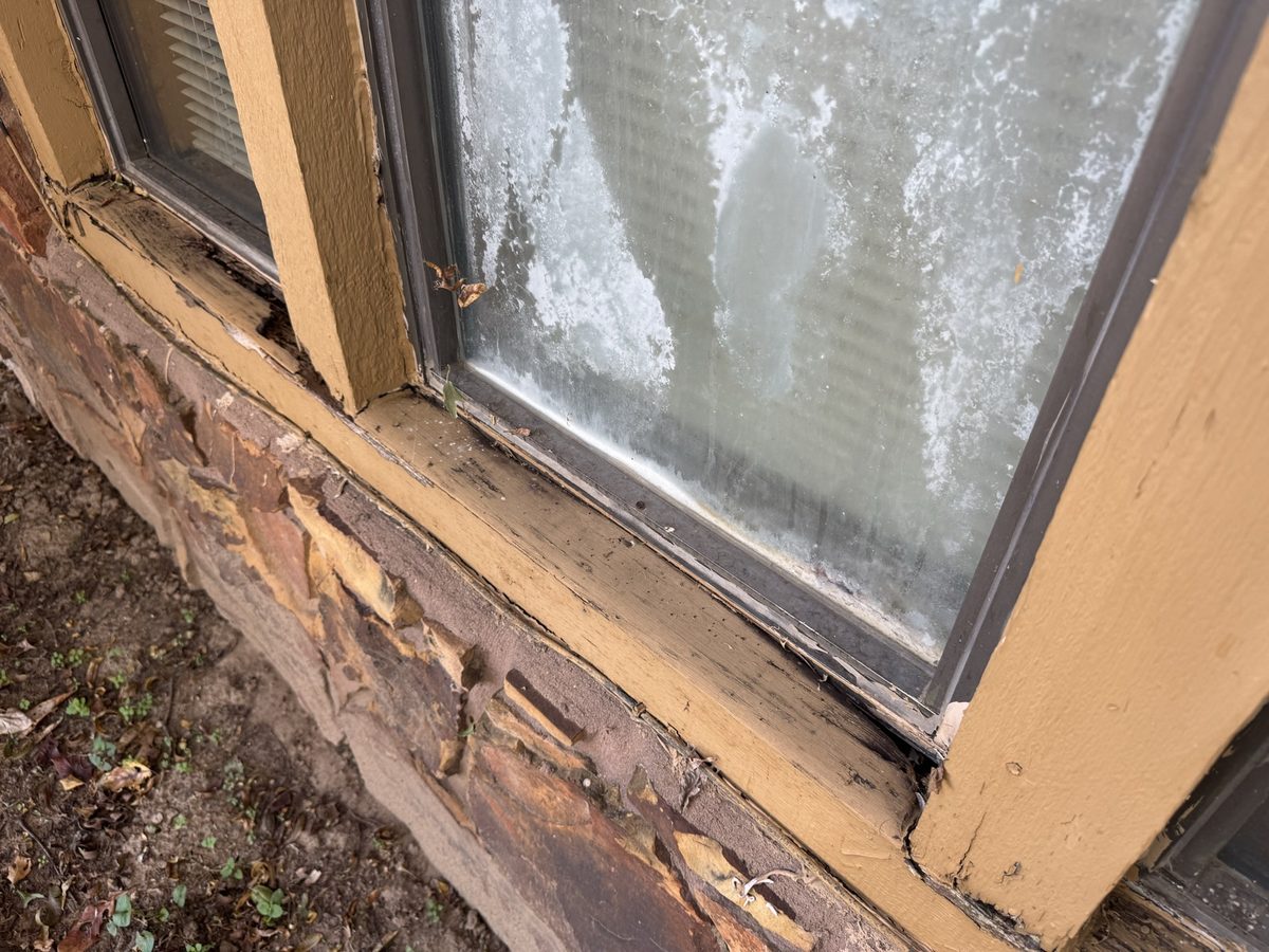 Double-pane window with white fog trapped between the panes above a cracked, peeling wood sill