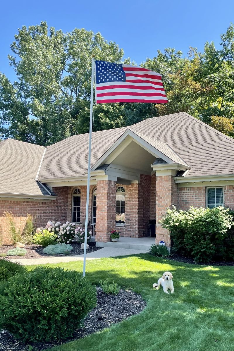 Ground set flagpole in front of a brick home