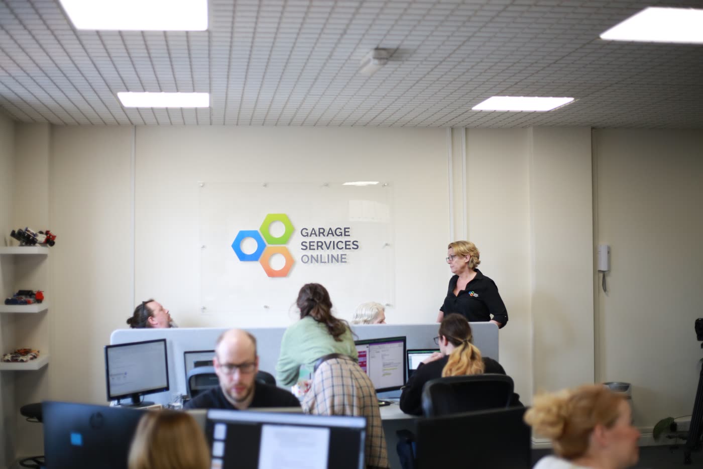 The Garage Services Online team at their desks, with the company logo on the office wall