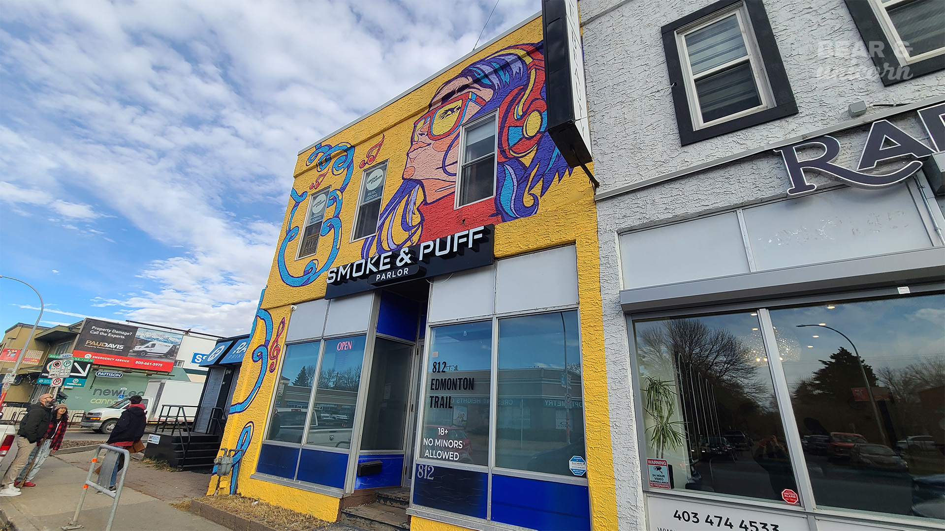 A wide-angle, low-elevation shot of the vibrant, completed yellow and blue mural on the building storefront under a blue sky. A wide-angle, low-elevation shot of the vibrant, completed yellow and blue mural on the building storefront under a blue sky.