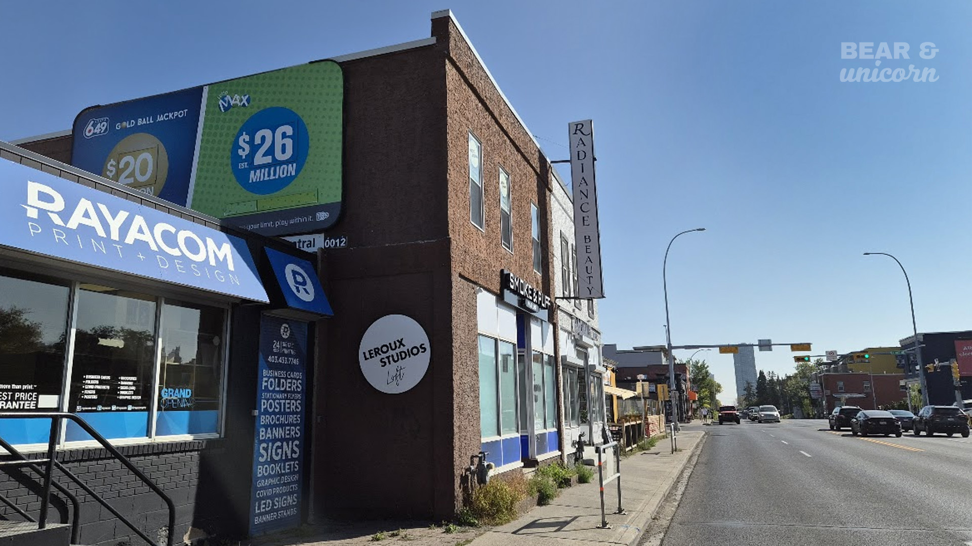 The corner building storefront before the mural was painted, featuring a grey facade with a Rayacom sign next to a street. The corner building storefront before the mural was painted, featuring a grey facade with a Rayacom sign next to a street.