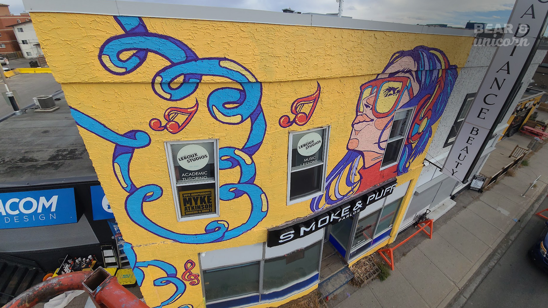 An elevated, high-angle view looking down at the freshly painted yellow mural on the building next to a busy city street. An elevated, high-angle view looking down at the freshly painted yellow mural on the building next to a busy city street.