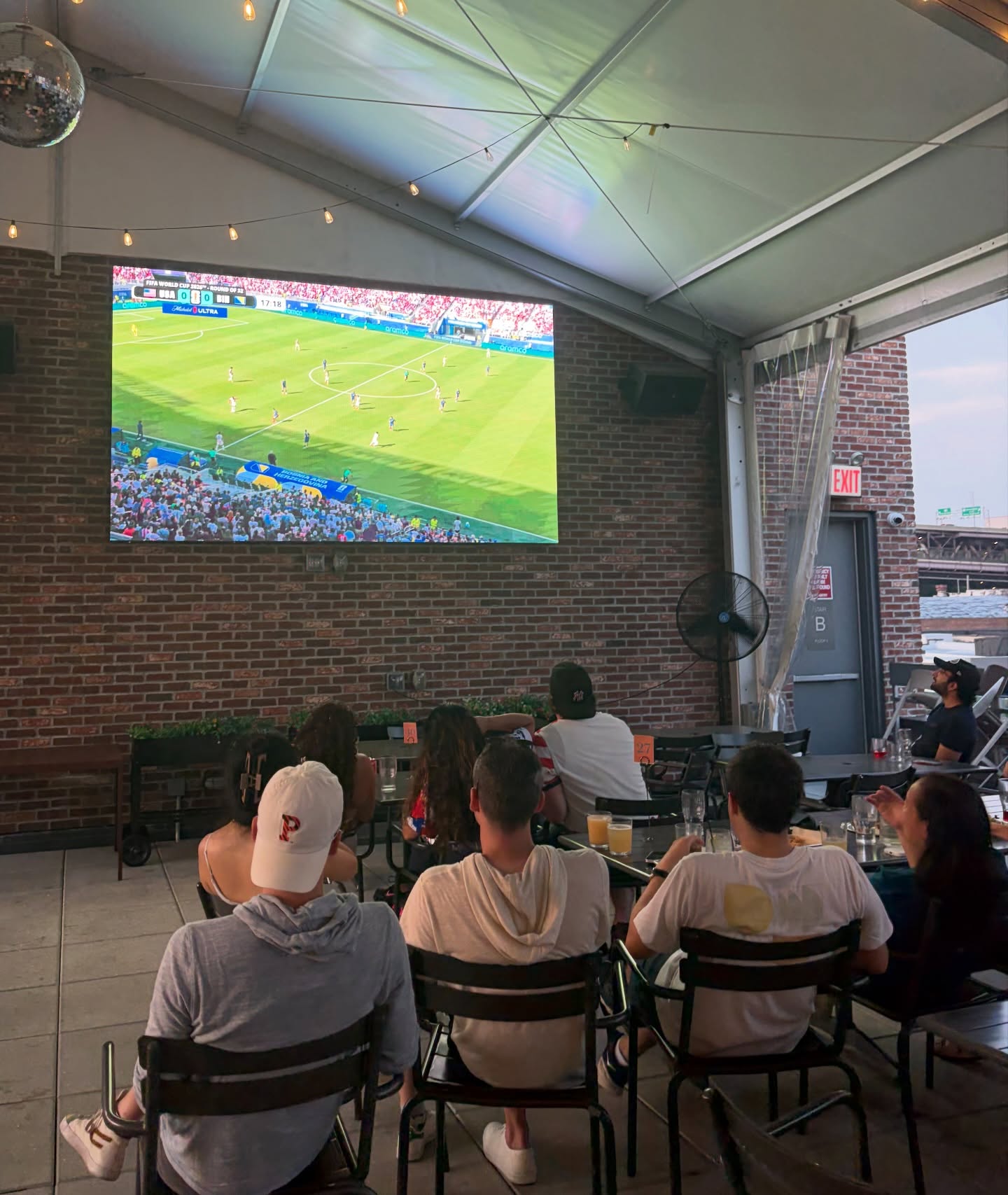 Restaurant patio filled with guests watching a live game on a giant YOLO outdoor screen