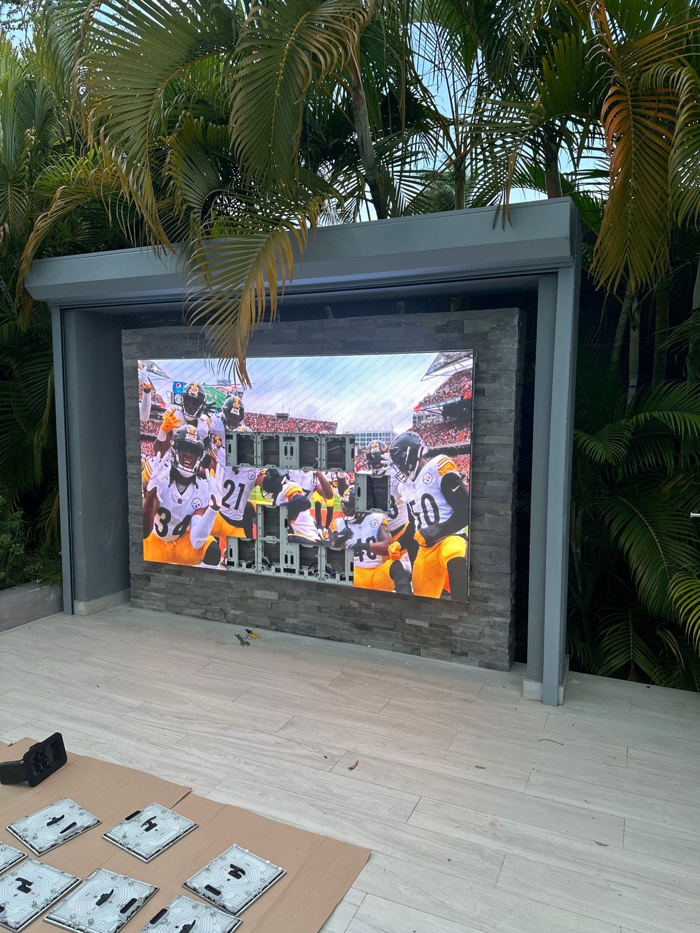 Large YOLO TV wall-mounted flush against an exterior wall above a backyard patio