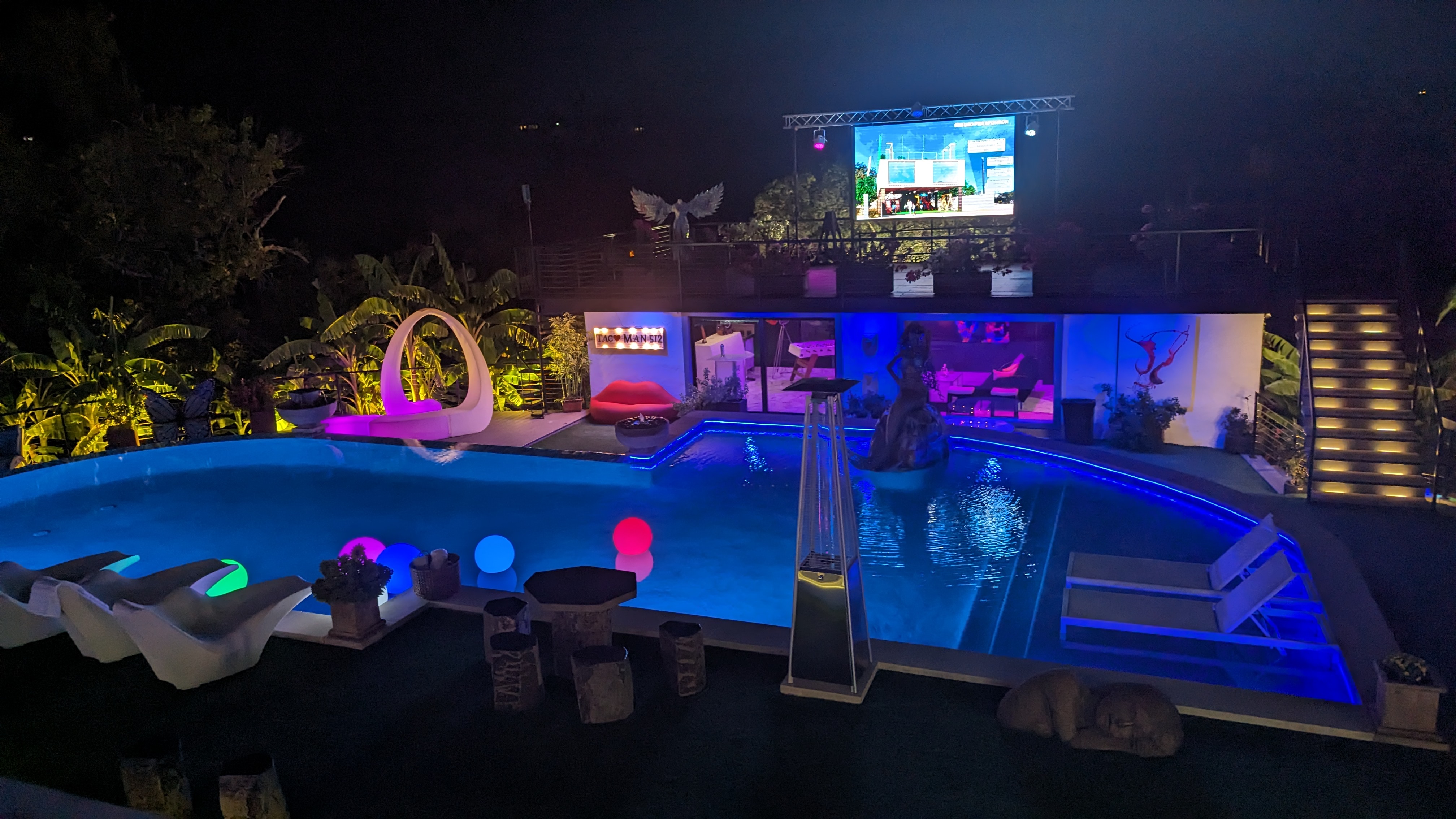 Evening gathering around the Austin YOLO TV with the pool and patio lit up after sunset
