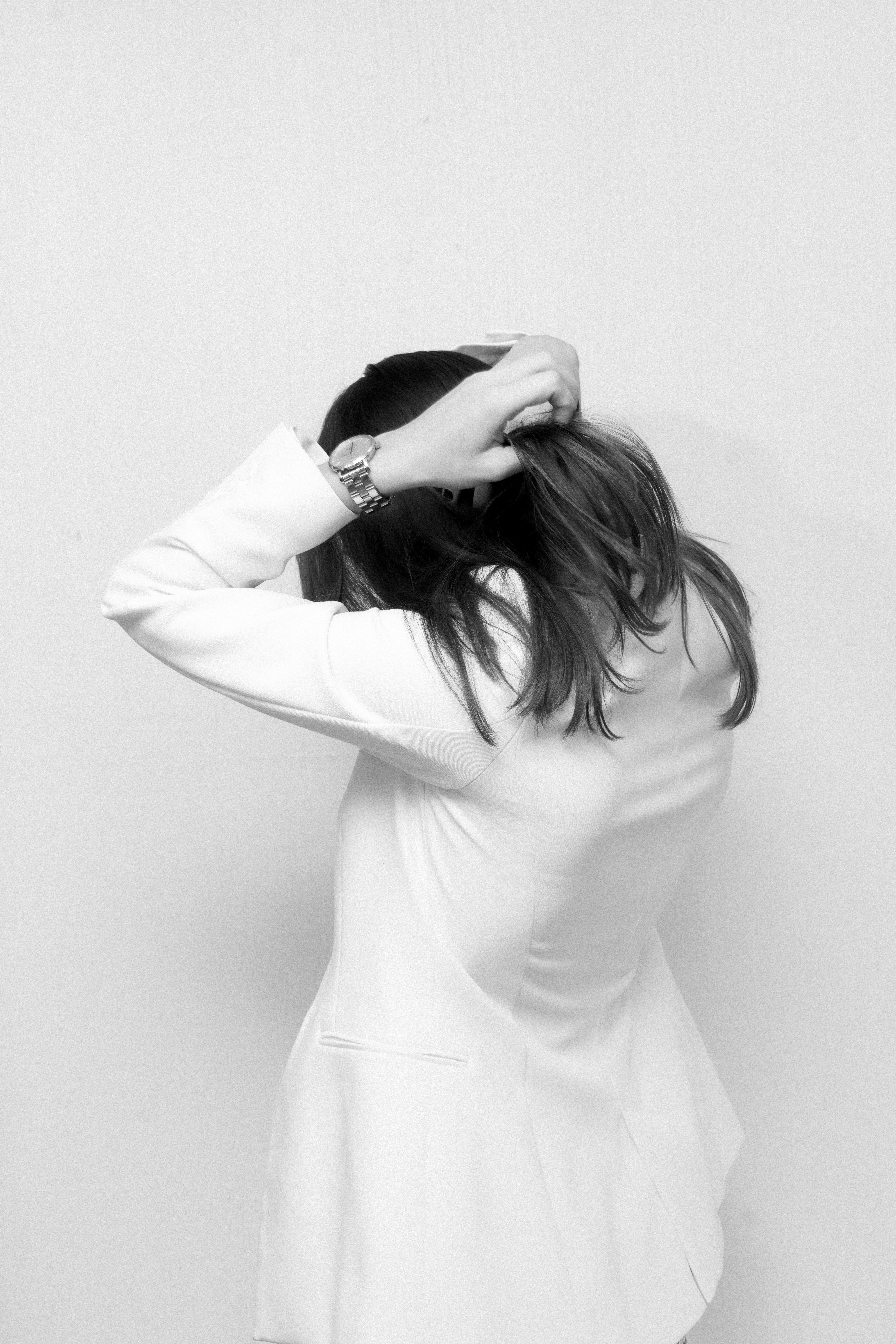 professional woman in a white blazer with hands above head in stressed posture holding head facing wall