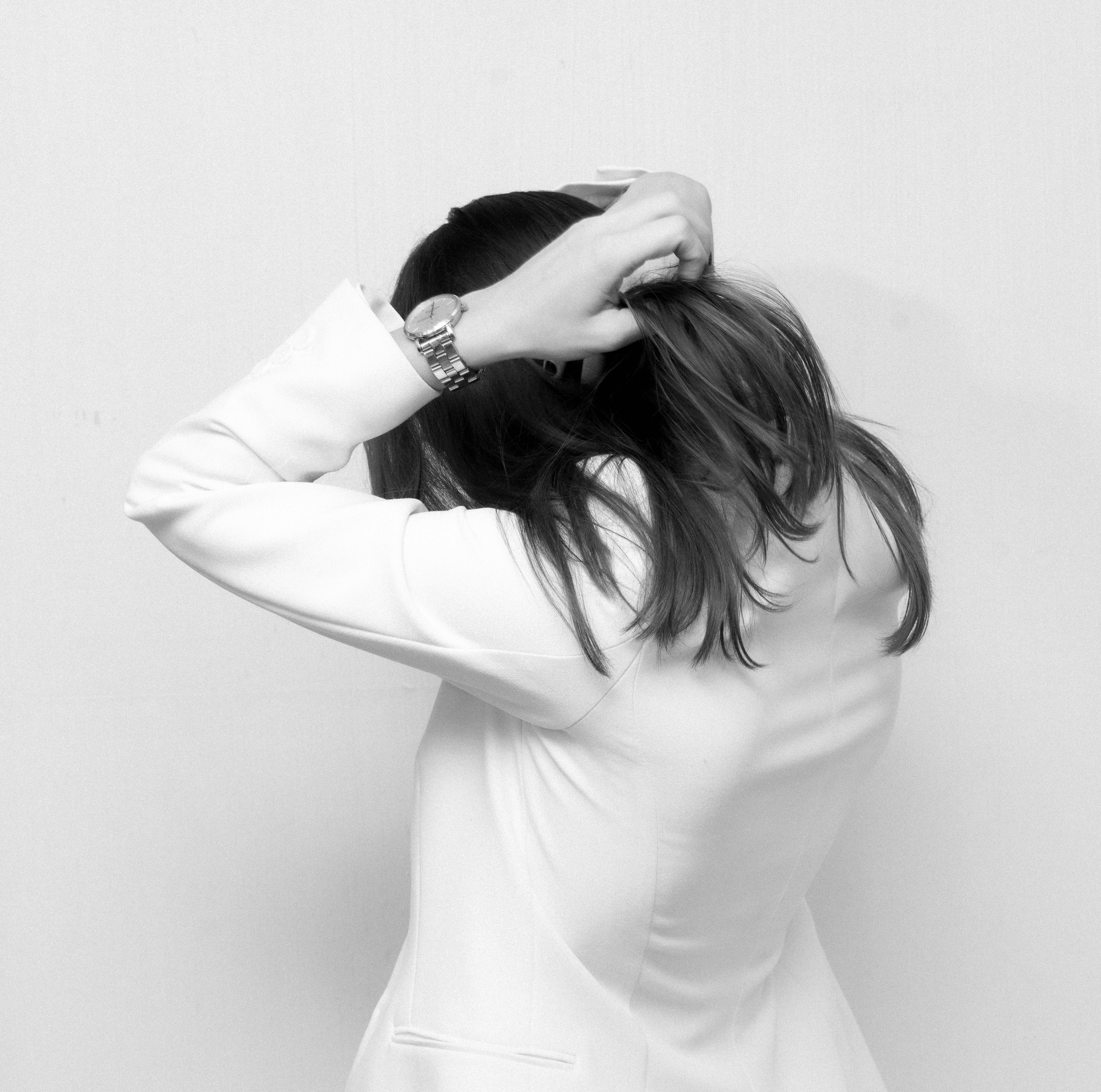 professional woman in a white blazer with hands above head in stressed posture holding head facing wall