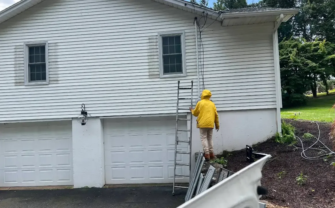 Painter on a ladder painting white siding on a Connecticut home