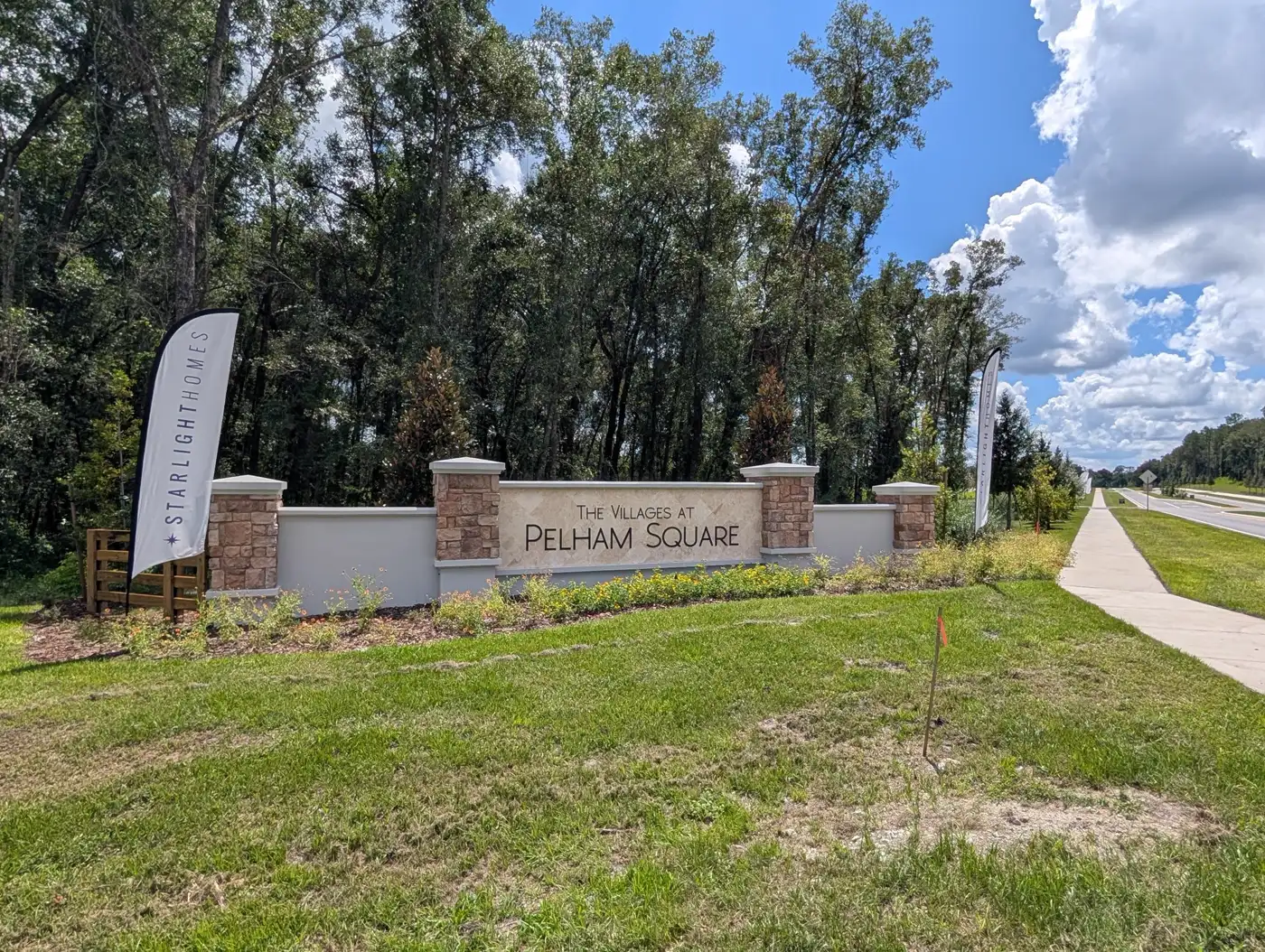 The Villages at Pelham Square entrance sign in DeLand, FL, with Starlight Homes flags and tall pines behind it