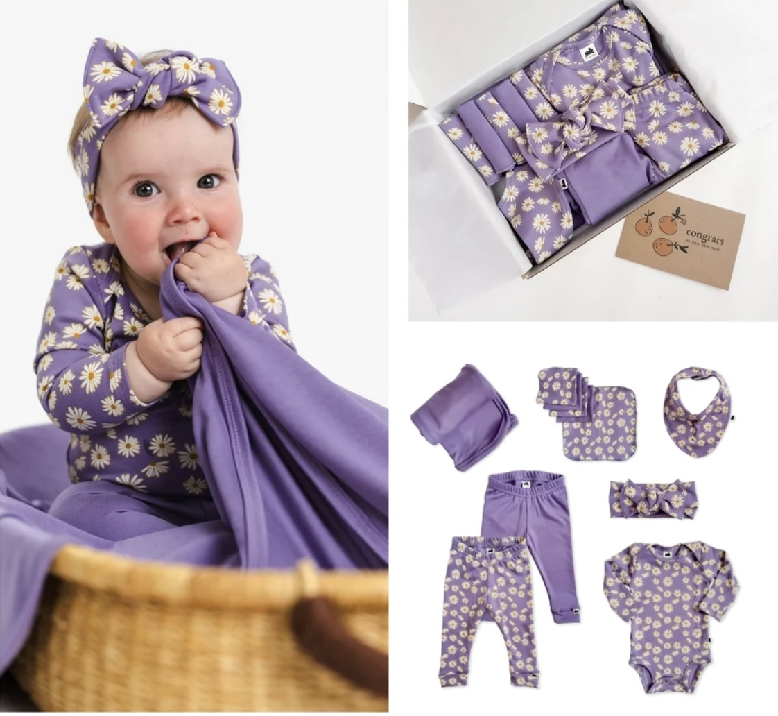 Baby wearing a purple floral outfit alongside matching baby clothing, accessories and a gift box
