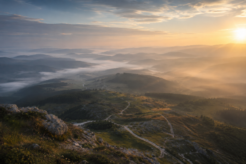 A high vantage point overlooking a varied landscape with winding terrain—hills, forest edges, and branching trails. A high vantage point overlooking a varied landscape with winding terrain—hills, forest edges, and branching trails.
