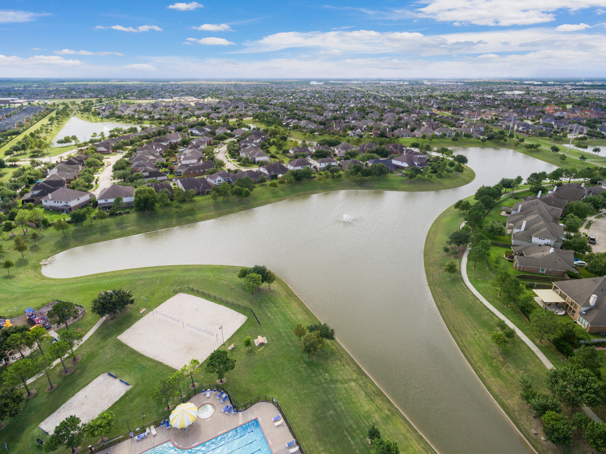 Aerial view of Shadow Creek Ranch in Pearland, Texas, showing lakes, waterfront homes, walking paths, a community pool, and volleyball courts.