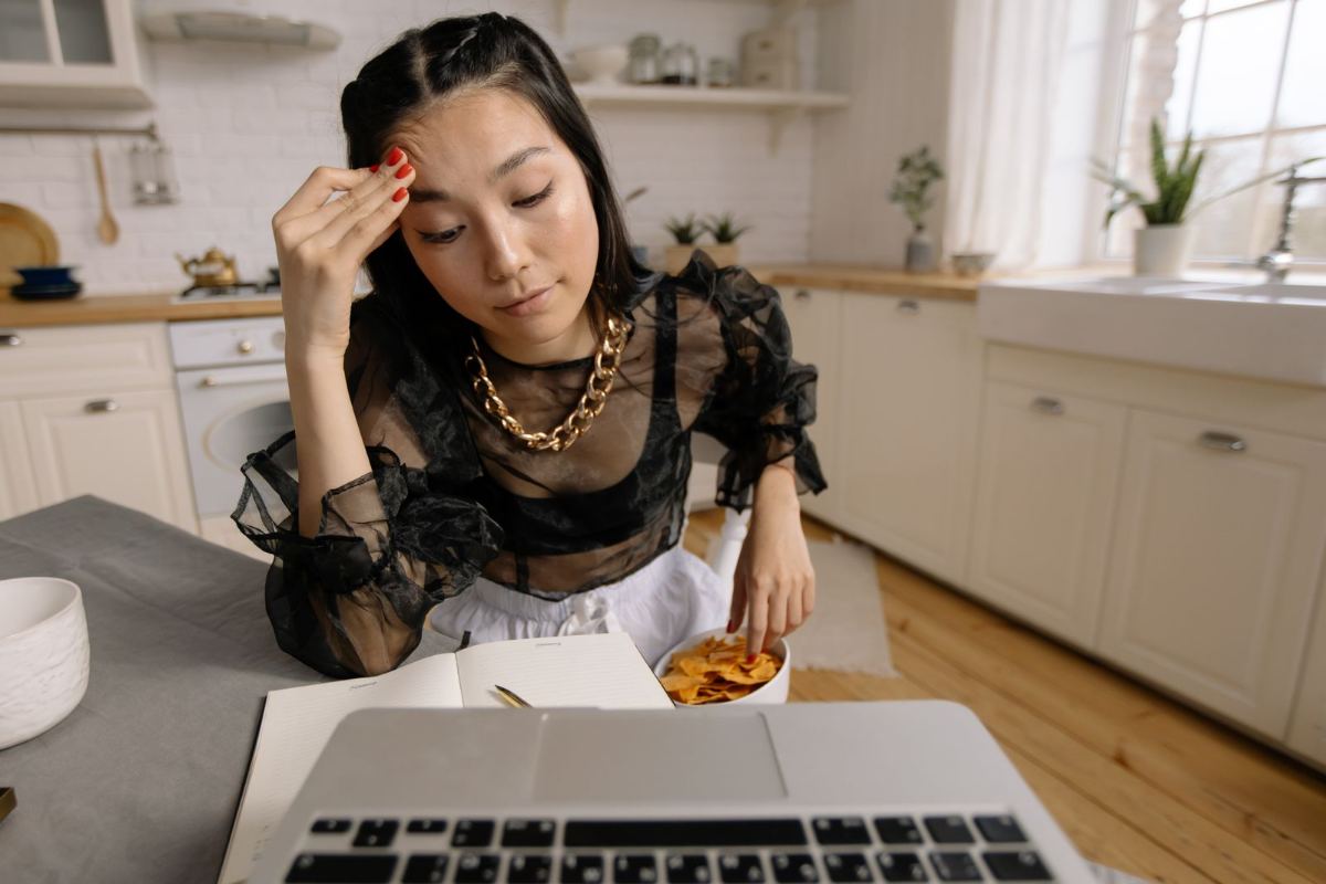 Tired woman at her kitchen table with a laptop and a bowl of snacks