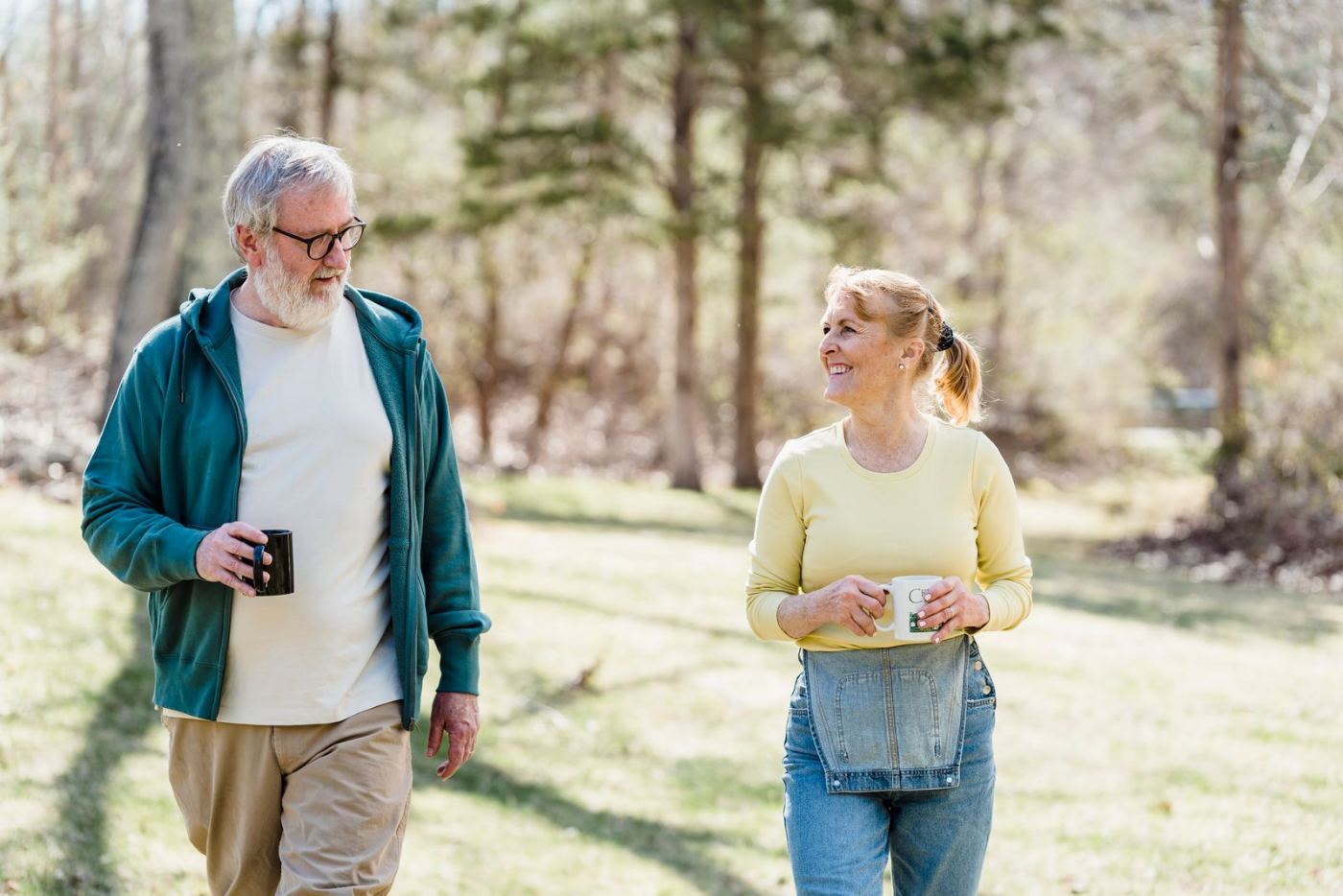 Smiling couple in their fifties walking outdoors with coffee mugs