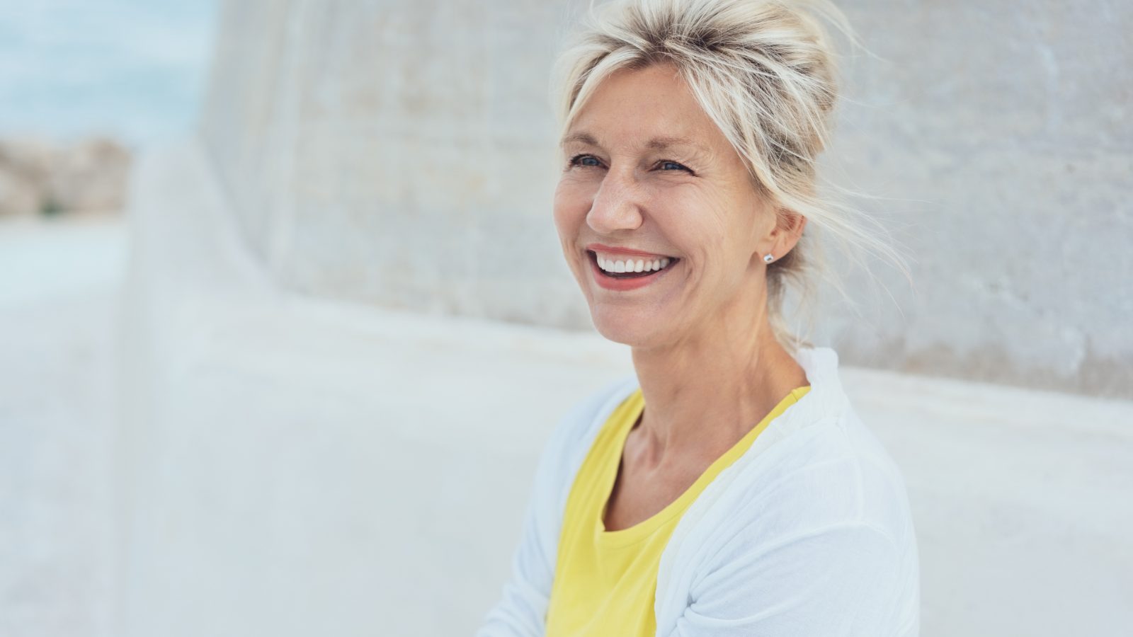 A woman in her fifties smiling, outdoors in bright light.