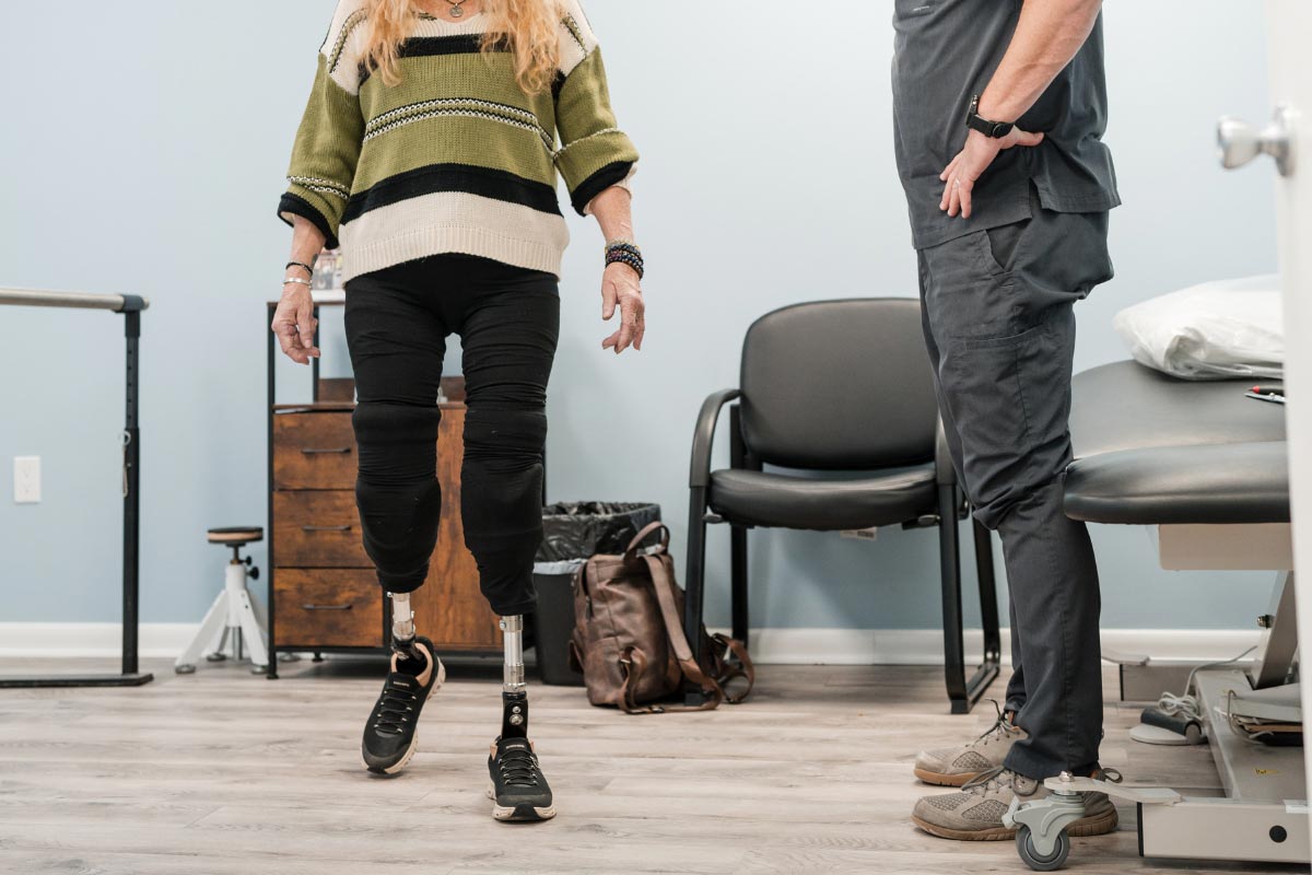 Patient practicing walking with bilateral prosthetic legs while a clinician monitors progress.
