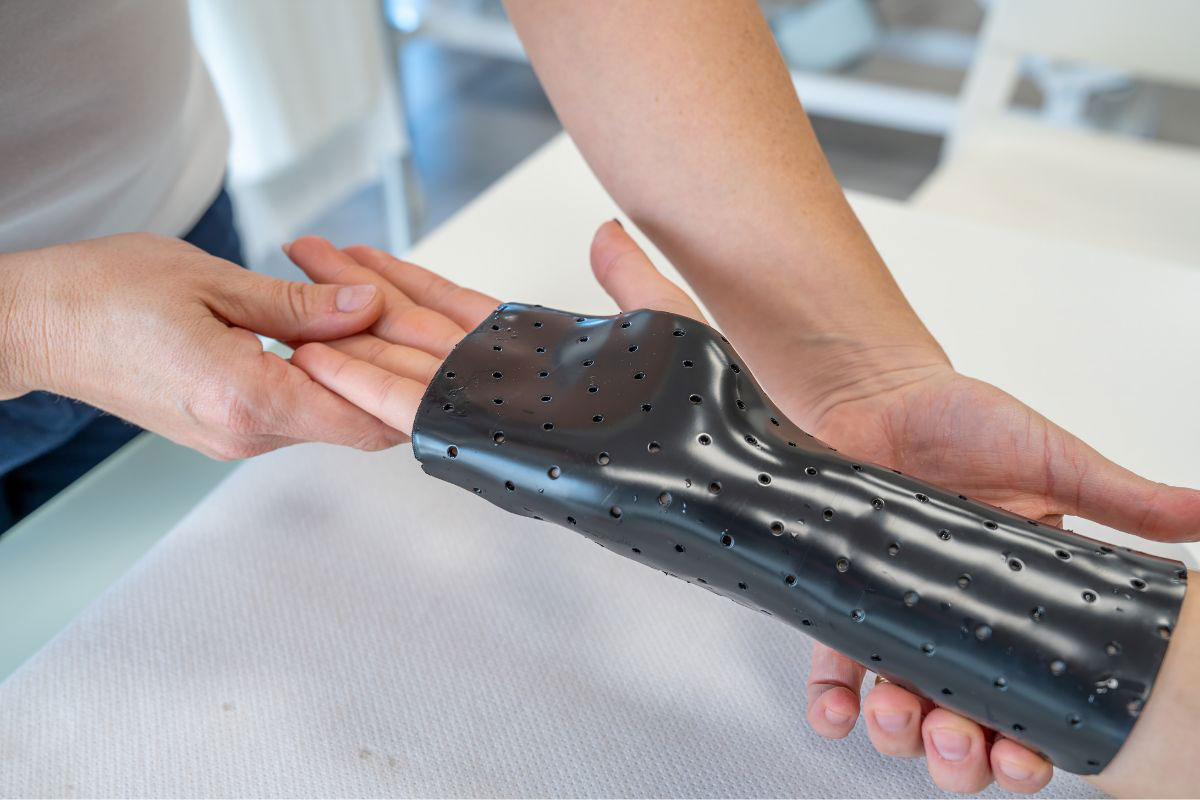 Orthotic specialist holding a patient's hand while carefully fitting a custom molded black plastic wrist brace. Orthotic specialist holding a patient's hand while carefully fitting a custom molded black plastic wrist brace.