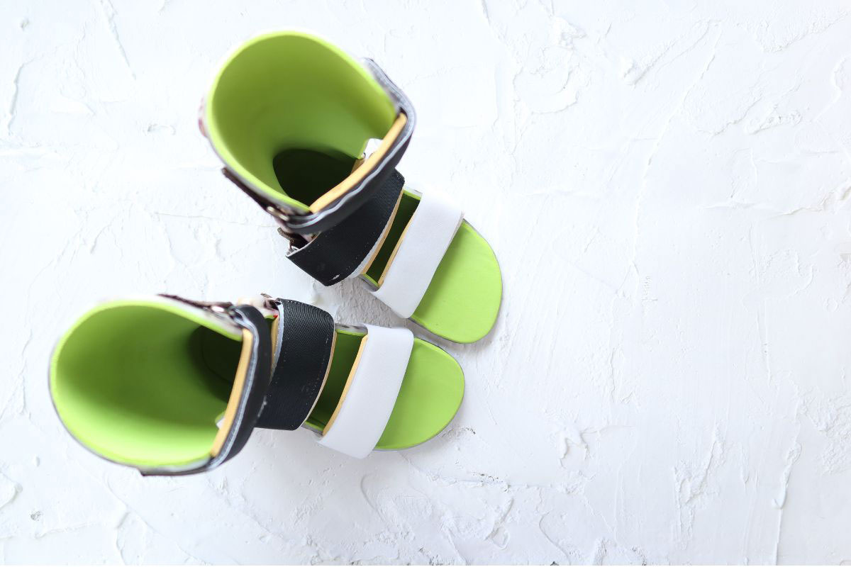 Top-down view of a pair of custom pediatric ankle-foot orthoses (AFOs) with bright green padding and black and white straps. Top-down view of a pair of custom pediatric ankle-foot orthoses (AFOs) with bright green padding and black and white straps.