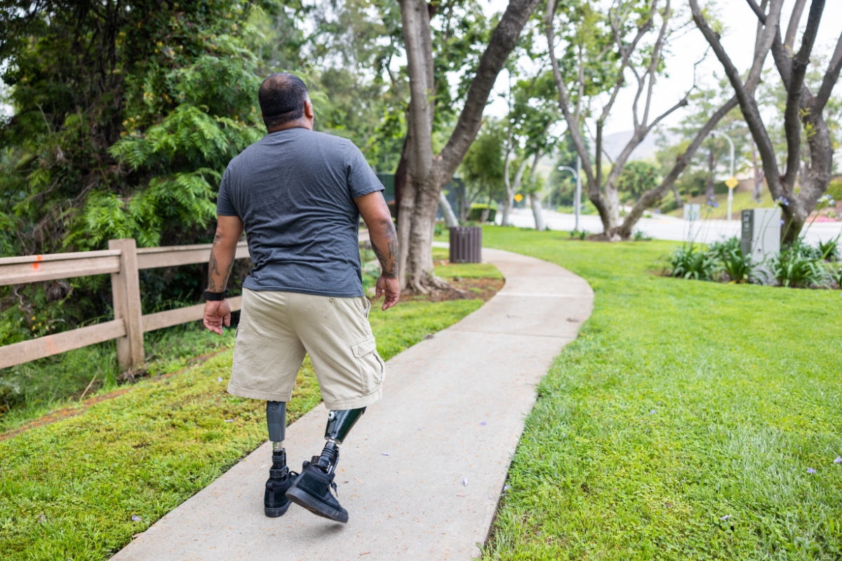 Man with bilateral leg prostheses walking along a paved outdoor path