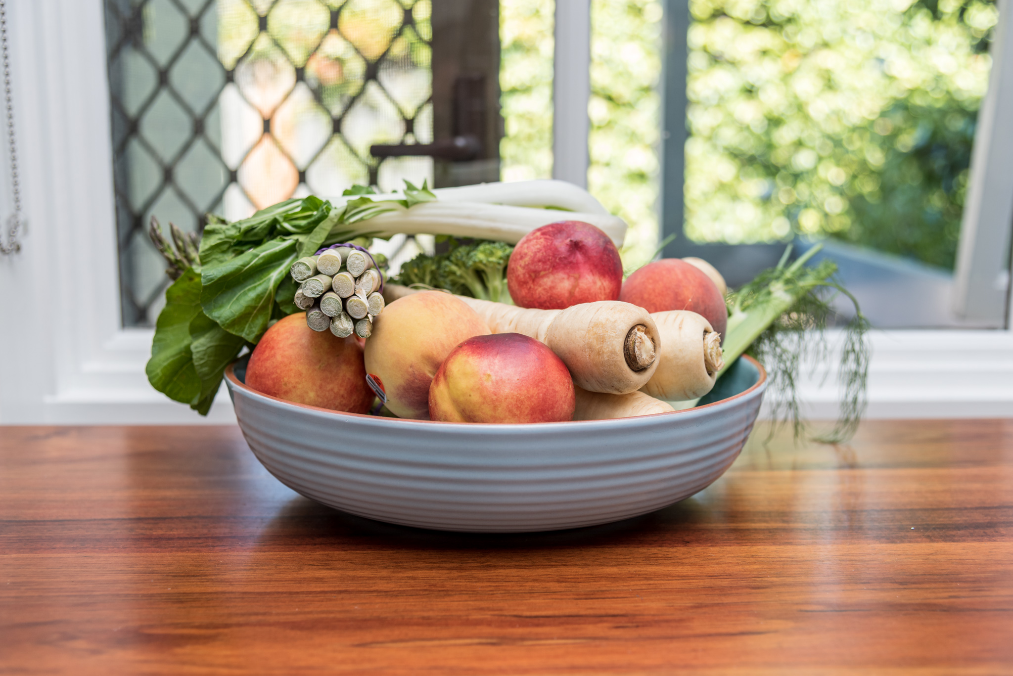 Fresh low histamine produce including nectarines, parsnips, asparagus and greens in a grey bowl