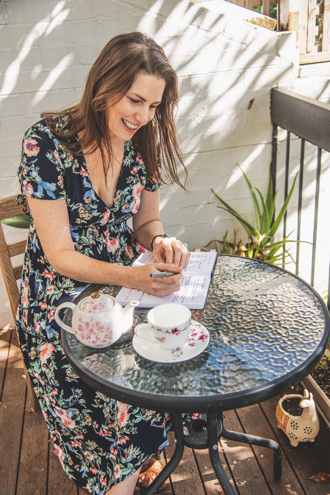 Luanne writing notes at a garden table with a cup of tea