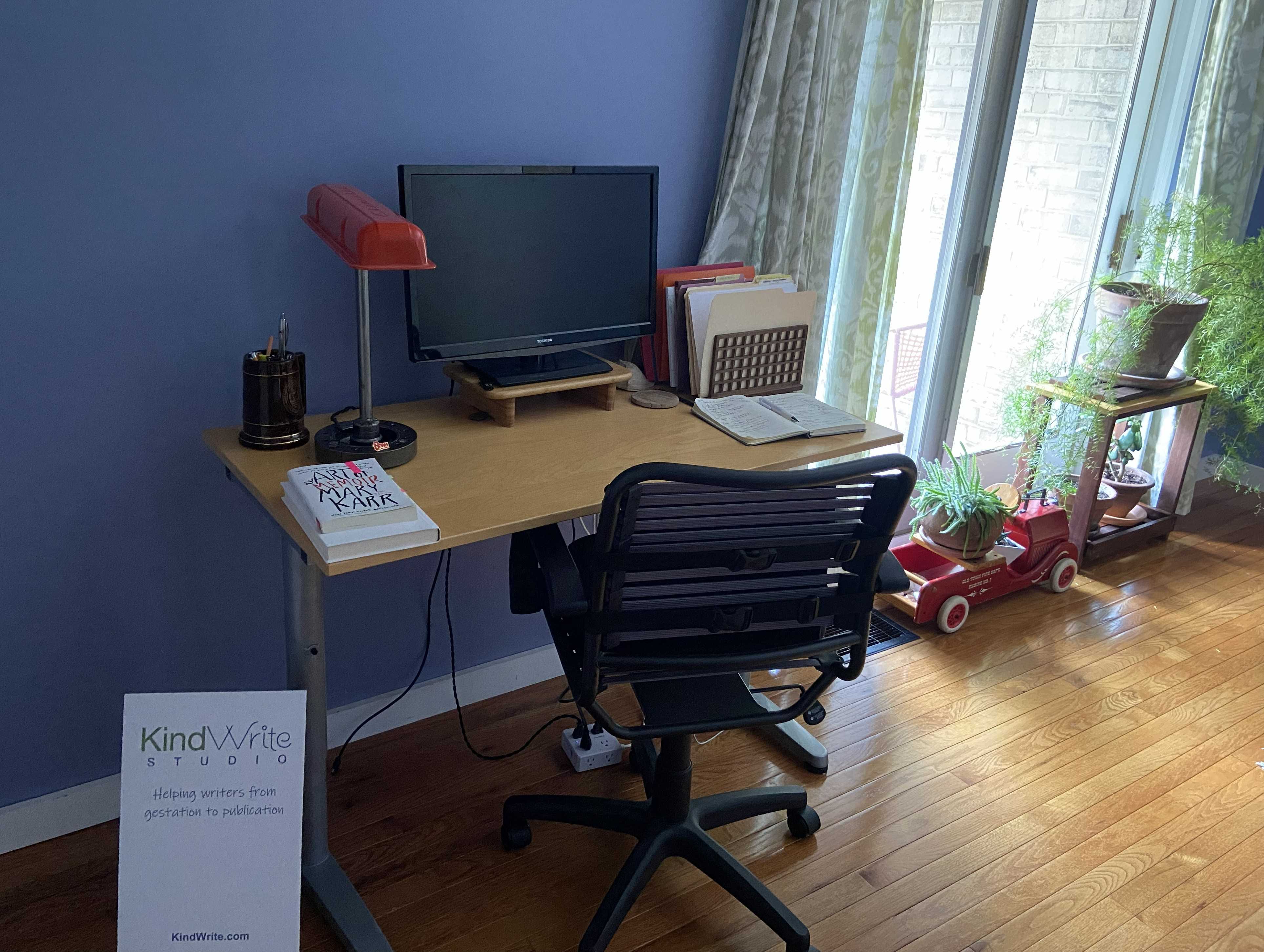 A writer's desk with a monitor, books and files in front of a window and plants A writer's desk with a monitor, books and files in front of a window and plants