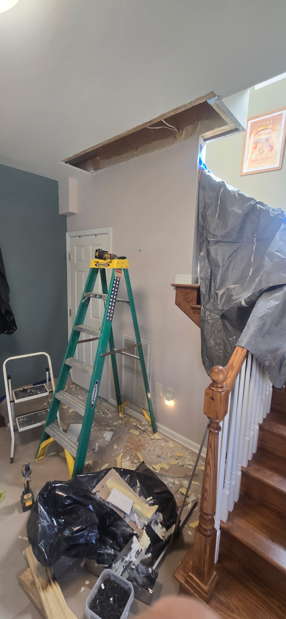 Hallway ceiling opened along a strip with the joists exposed, stairs sheeted off and debris bagged