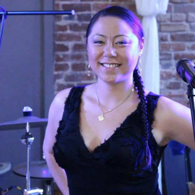 Eu Yu smiling, arms folded, with a drum kit behind her.