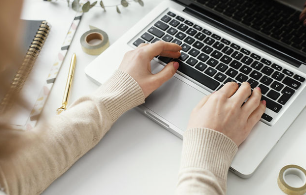 Person typing on a laptop at a desk with notebooks and stationery, illustrating the preparation and research stage of creating strategic content with AI.