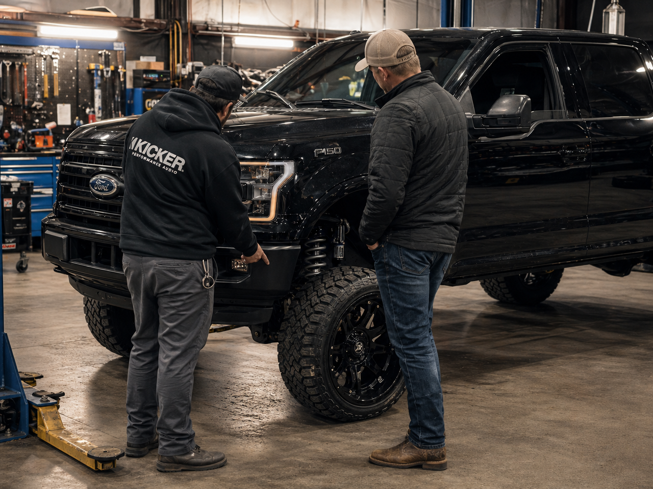 Builder and customer in conversation beside a lifted truck in the shop bay discussing a build commission