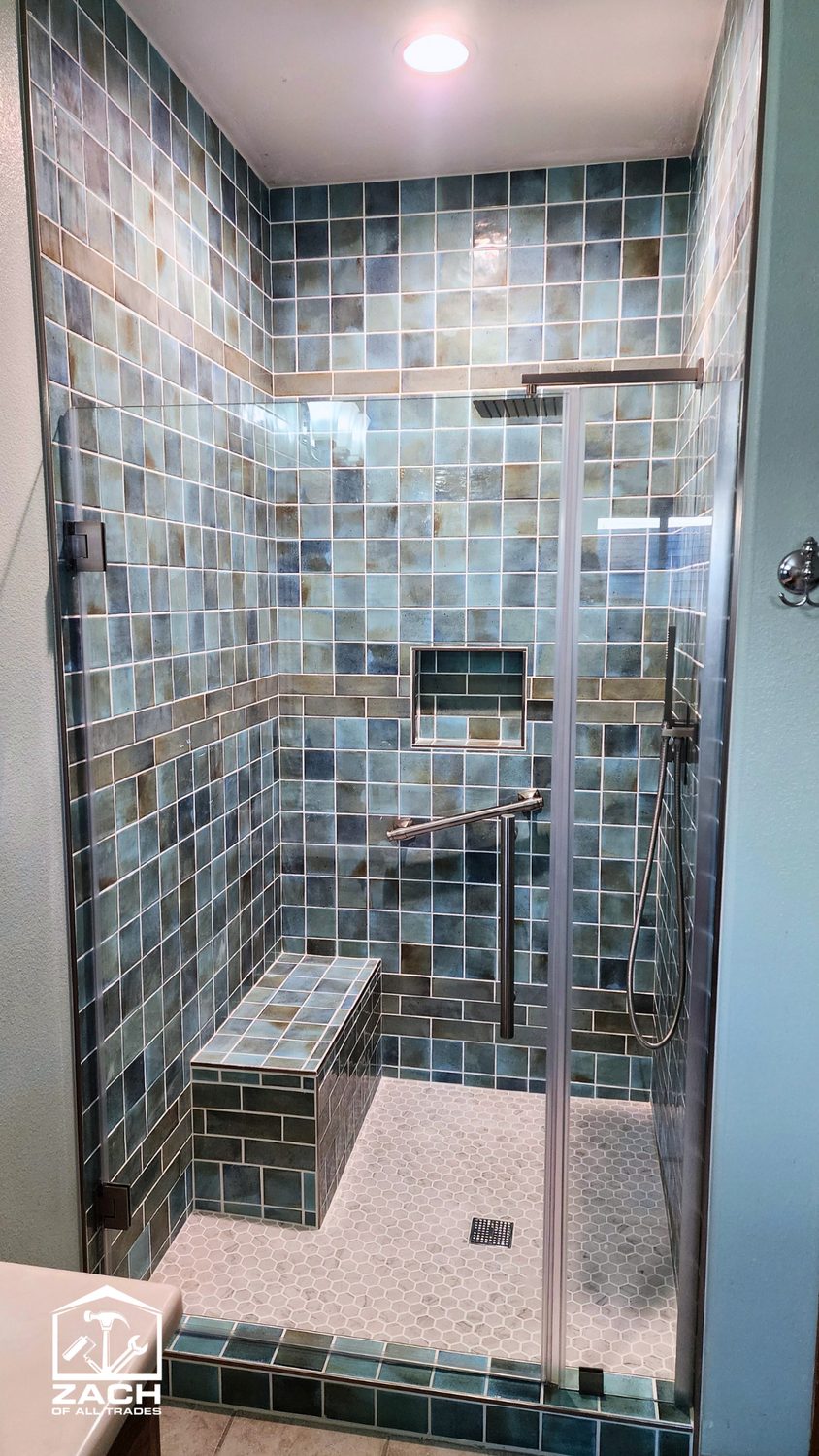 Blue and teal glass-tile walk-in shower with a built-in bench and niche