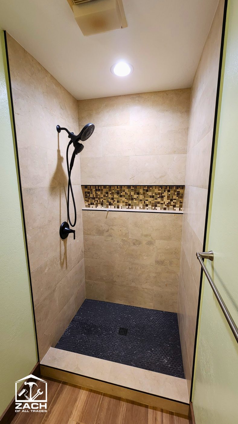 Cream tile walk-in shower with glass-mosaic accent band and pebble floor