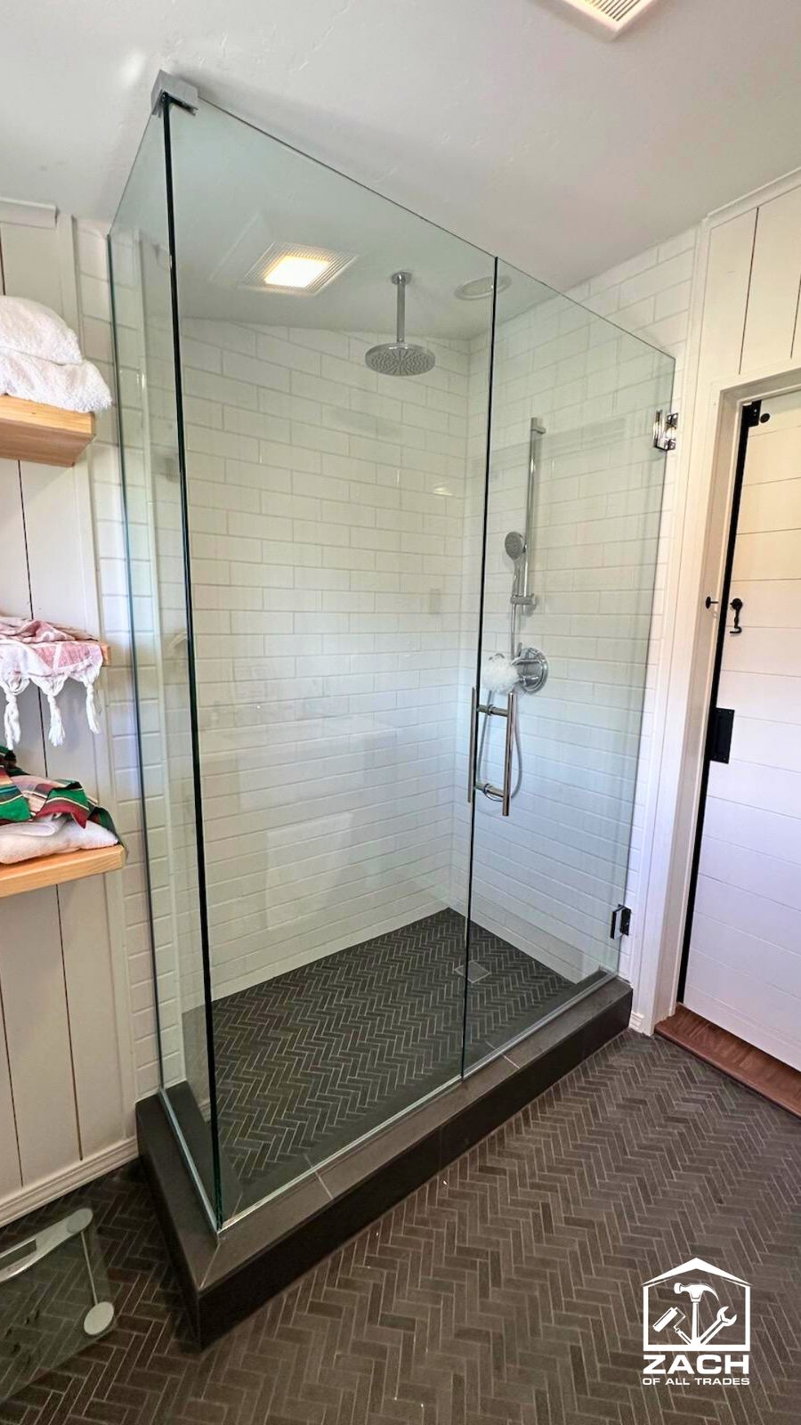 Finished white subway-tile walk-in shower with frameless glass and a herringbone floor
