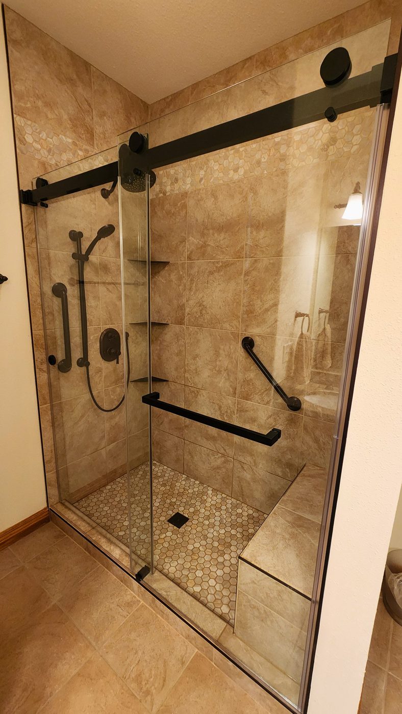 Travertine-look tile shower with black glass barn-door enclosure and bench